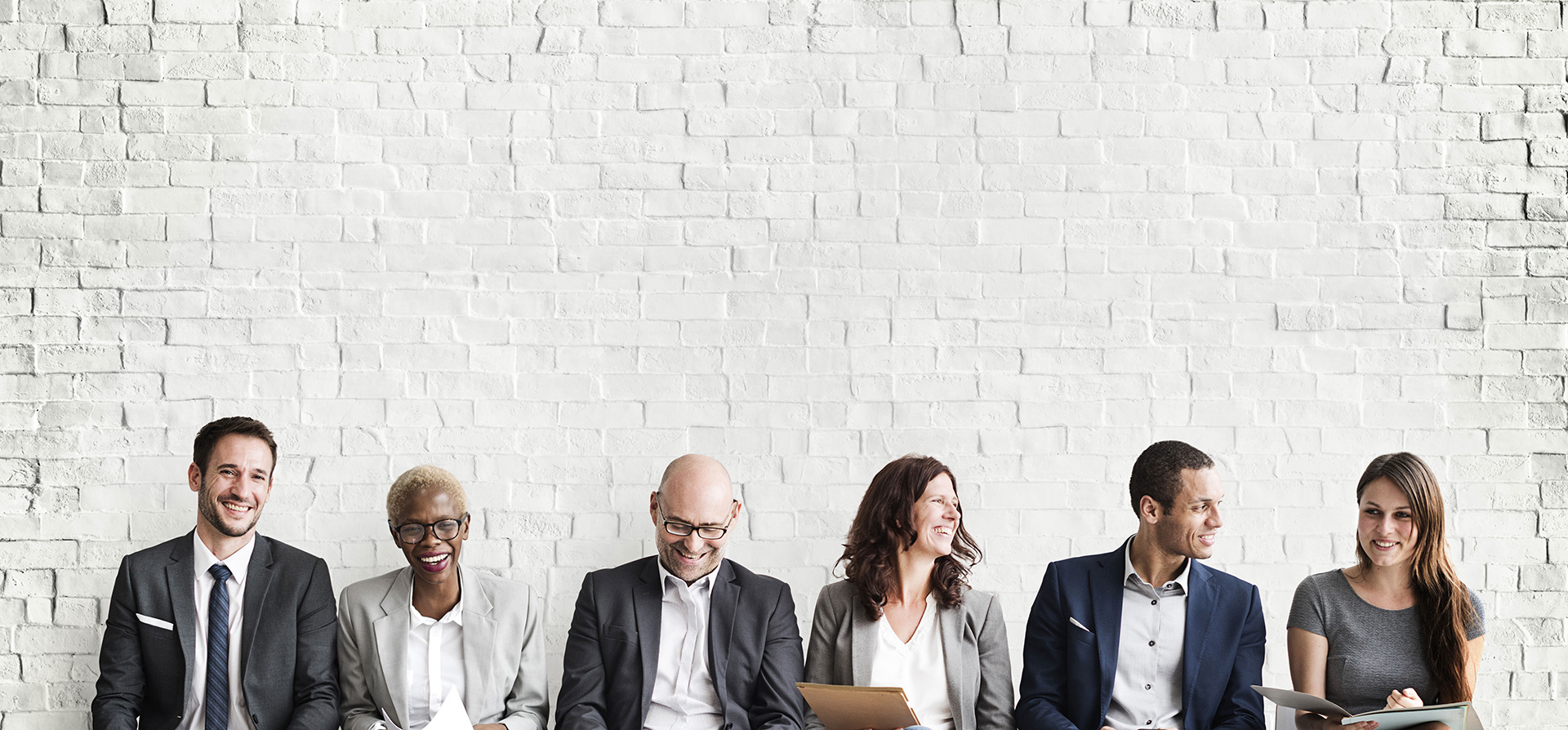 Diverse group of professionals smiling and sitting against a white brick wall.