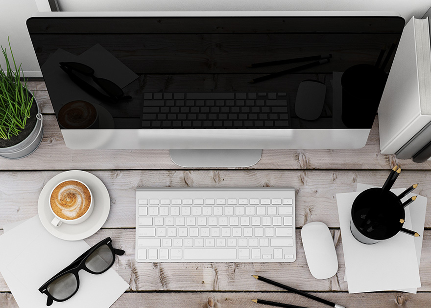 Neat workspace with a computer, coffee, glasses, and pencils on a wooden desk.