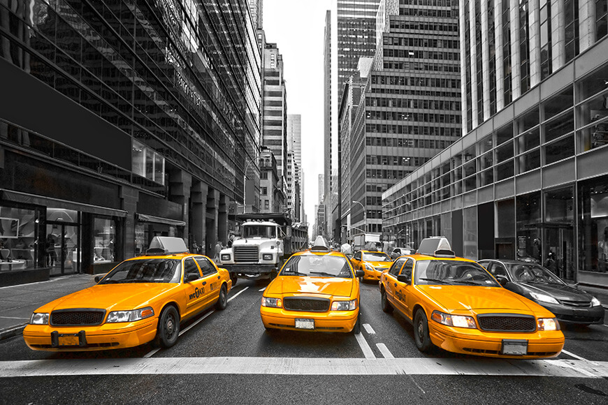 Bright yellow taxis stand out in a black-and-white city street scene.