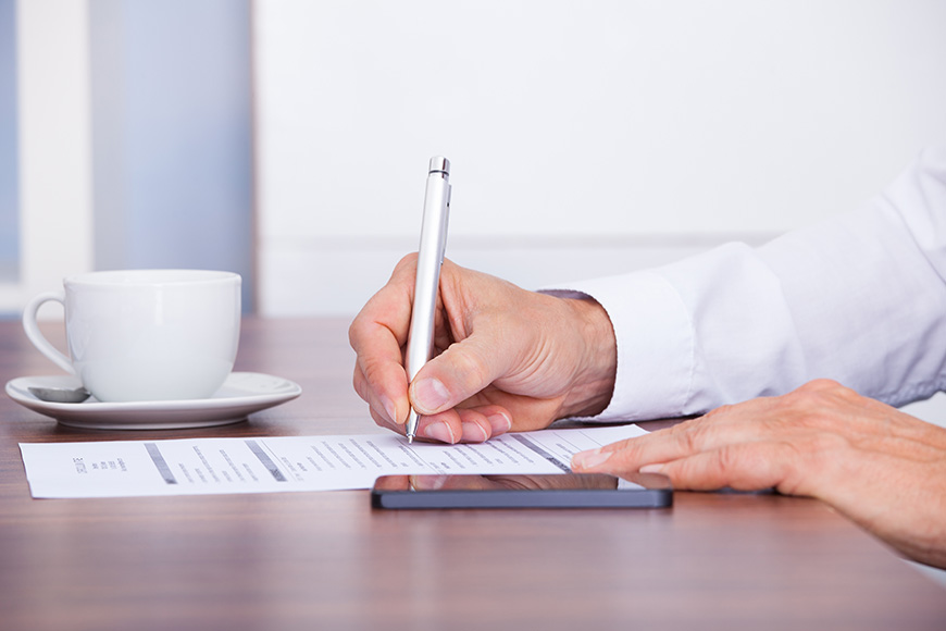 Person signing a document with a pen at a desk.