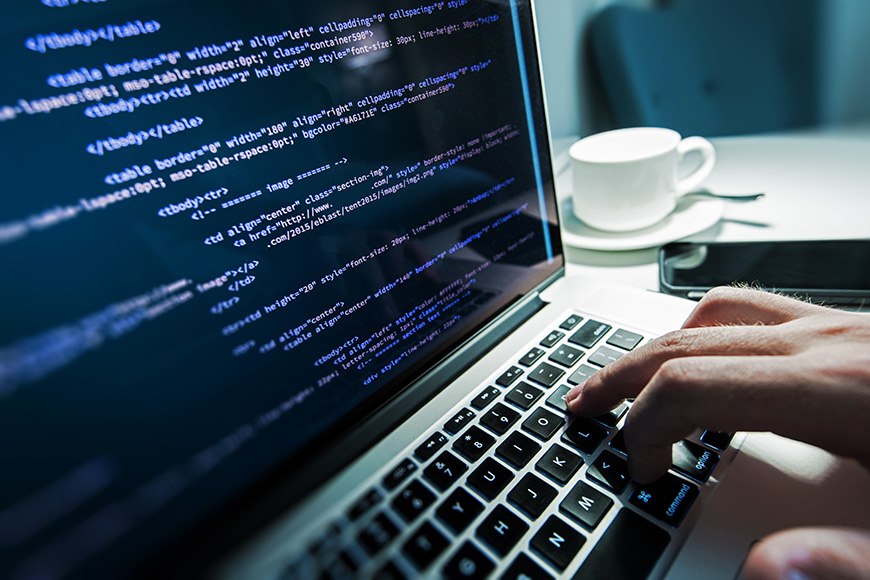 Person typing HTML code on a laptop with a coffee cup nearby.
