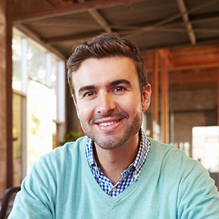 Smiling man in a casual sweater and checkered shirt.