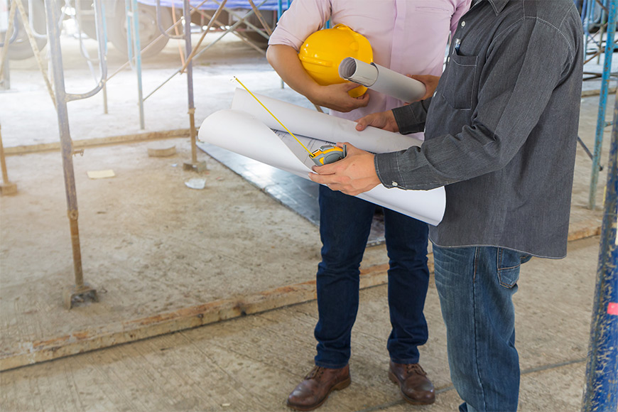 Two construction workers reviewing blueprints on a building site.