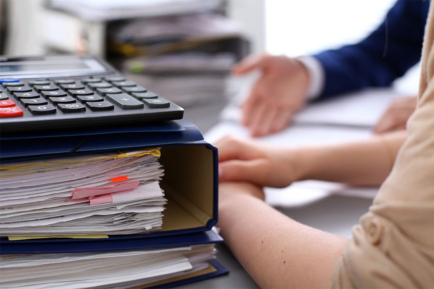 Stack of binders and calculator on desk during office discussion.