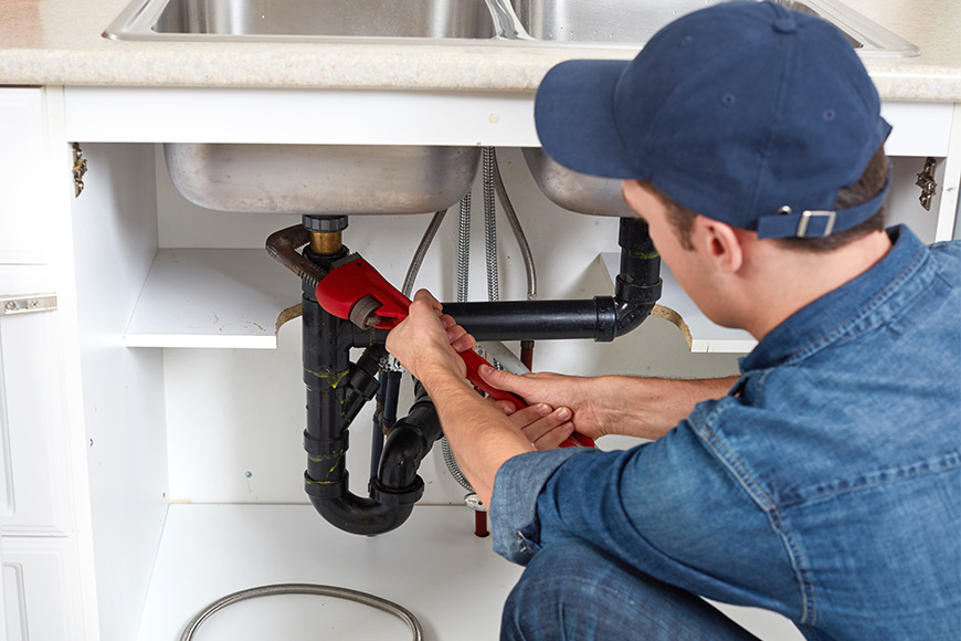 Plumber fixing sink pipes with a wrench under the kitchen cabinet.