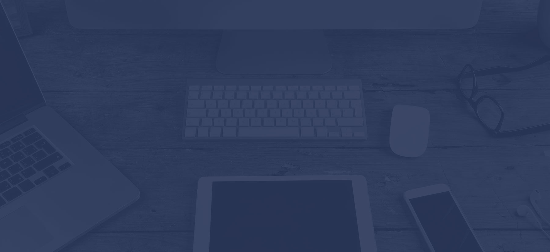 A workspace with various electronic devices and glasses on a wooden table.