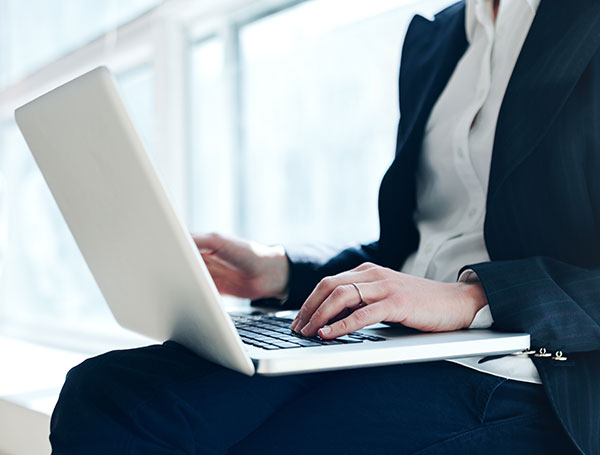 Person typing on a laptop while wearing a suit jacket and white shirt.