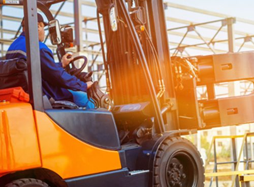 Worker operating an orange forklift outdoors.