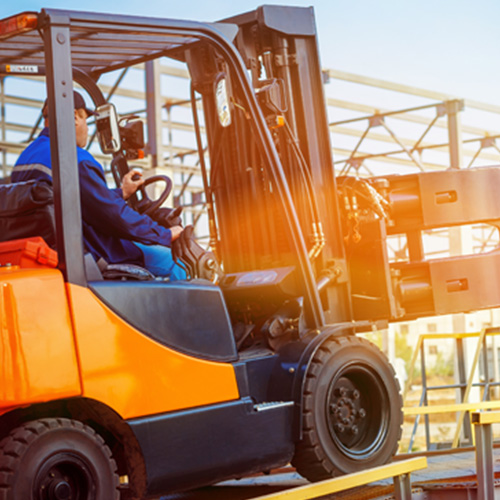 A worker operates an orange forklift under a clear sky.
