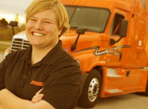 Smiling person with arms crossed standing in front of an orange truck.