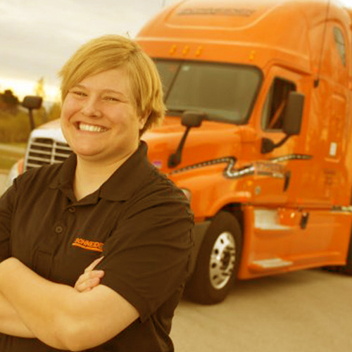 Smiling person with arms crossed standing in front of an orange truck.