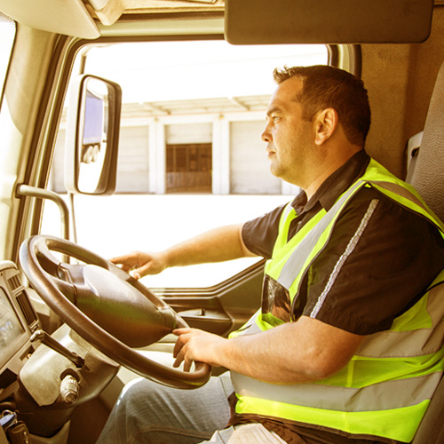 Truck driver in a high-visibility vest driving a large vehicle.