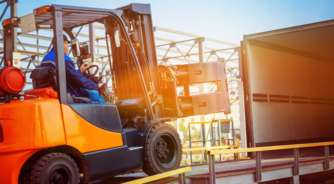 Forklift operator handling cargo in an industrial setting at sunset.
