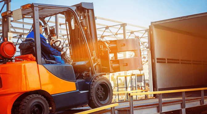 Forklift operator handling cargo in an industrial setting at sunset.